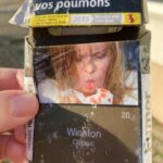 A graphic cigarette pack thrown on the ground in Hoenheim, north of Strasbourg, France. Most cigarettes come from Germany, where they are cheaper because they are taxed less than in France. Germany is just over the bridge from Strasbourg. There are a lot of smokers in France, who seem undeterred by the images, and who also disproportionately throw litter on the ground. Was tut man? Do you want to cough up blood like this woman?