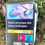 "Smoking provokes cardiac crises." A graphic cigarette pack thrown on the ground in Hoenheim, north of Strasbourg, France. Most cigarettes come from Germany, where they are cheaper because they are taxed less than in France. Germany is just over the bridge from Strasbourg. There are a lot of smokers in France, who seem undeterred by the images, and who also disproportionately throw litter on the ground. Was tut man? The sad man on this pack is having his heart restarted..