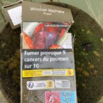 "Smoking causes 9 out of 10 lung cancers." A graphic cigarette pack thrown on the ground in Hoenheim, north of Strasbourg, France. Most cigarettes come from Germany, where they are cheaper because they are taxed less than in France. Germany is just over the bridge from Strasbourg. There are a lot of smokers in France, who seem undeterred by the images, and who also disproportionately throw litter on the ground. Was tut man? The picture shows lung surgery in progress.