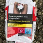 "Smoking augments the risk of impotency," in both French and German. A graphic cigarette pack thrown on the ground in Hoenheim, north of Strasbourg, France. Most cigarettes come from Germany, where they are cheaper because they are taxed less than in France. Germany is just over the bridge from Strasbourg. There are a lot of smokers in France, who seem undeterred by the images, and who also disproportionately throw litter on the ground. Was tut man? The sad man on this pack might as well have his potency destroyed.
