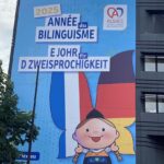 Banner outside of the Alsatian government building in Strasbourg. The traditional language is Alsatian, similar to German, but the official language is French. The girl's headdress is in the shape of the traditional Alsatian bonnet and sports the colors of France and of Germany. The symbol for Alsace looks like a traditional Alsatian pretzel.