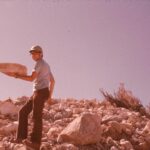 The photographer, Stan Rice, is not as strong as he appears when holding a boulder in one hand. The boulder is diatomaceous earth (diatomite), created by the slow accumulation of dead diatoms off the Pacific coast near Lompoc north of Santa Barbara in California. The diatomite rock was lifted by the San Andreas fault above sea level about a million years ago. Diatomite is much lighter than rock. It is mined industrially, hence the requirement for a hard hat. Photo 1978.